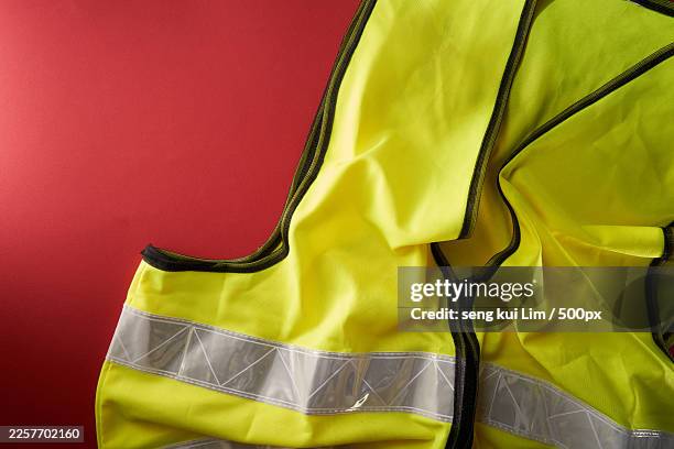 high visibility vest on a red background, symbolizing safety and caution - material reflector de seguridad fotografías e imágenes de stock