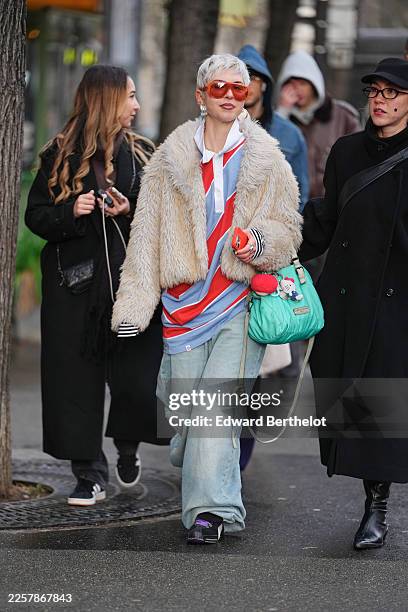 Guest wears a short platinum blond pixie haircut with a textured top, oversized orange tinted aviator sunglasses, metal hoop earrings, a green...