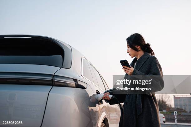 happy woman charging her electric car in urban setting at sunset - plugging in stock pictures, royalty-free photos & images