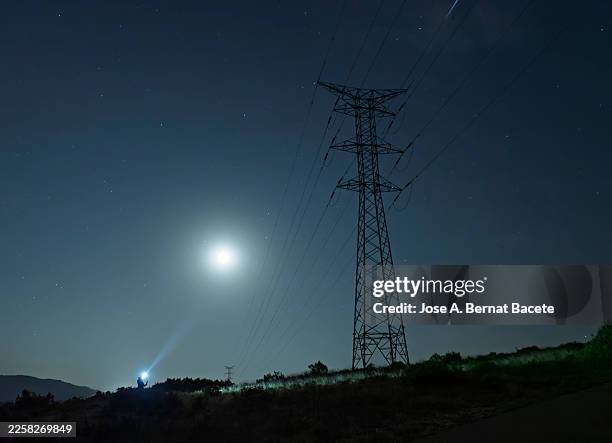 a high-voltage tower on a mountain with an electrician carrying flashlights repairing a fault at night. - iberian peninsula stock pictures, royalty-free photos & images