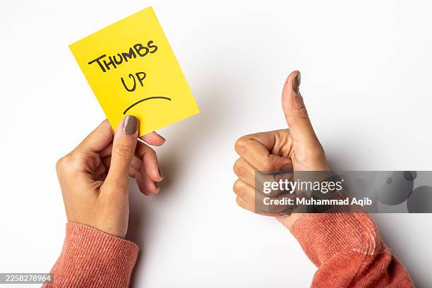 hands show a thumbs up with a yellow sticky note expressing approval in a simple setting - feedback loop stock pictures, royalty-free photos & images