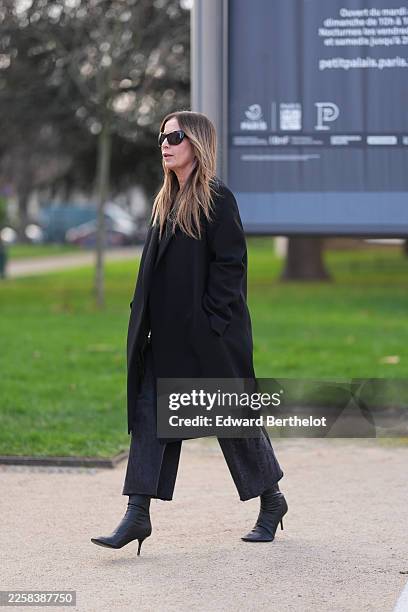 Guest wears long straight brown hair with lighter blonde highlights in a center part, black oversized sunglasses, a black wool coat with a notched...