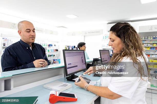 female pharmacists serving and collecting payments from customers at the pharmacy counter - woman at pharmacy stock pictures, royalty-free photos & images