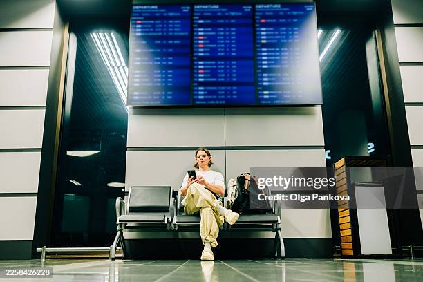man traveling sitting at airport using smartphone - commodité photos et images de collection