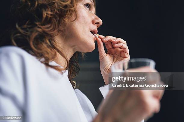 woman taking pill with glass of water - europese etniciteit stockfoto's en -beelden