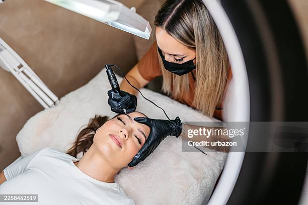 jeune femme se faisant tatouer les sourcils par une technicienne des sourcils dans un salon de beauté - maquillage permanent photos et images de collection