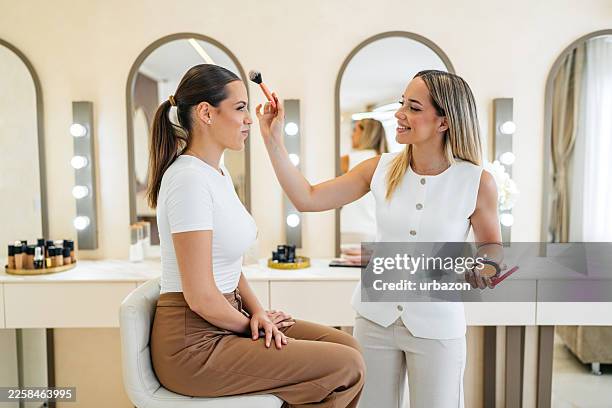 jeune femme se faisant maquiller par une esthéticienne dans un salon de beauté - maquillage professionnel photos et images de collection