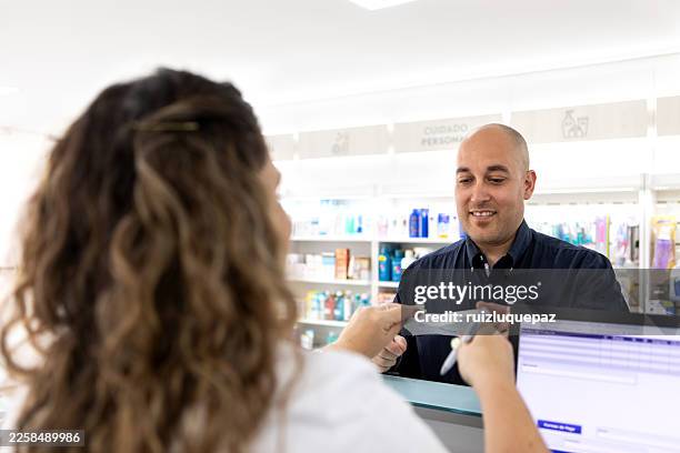 female pharmacist serving and collecting payments from customers at the pharmacy counter - woman at pharmacy stock pictures, royalty-free photos & images