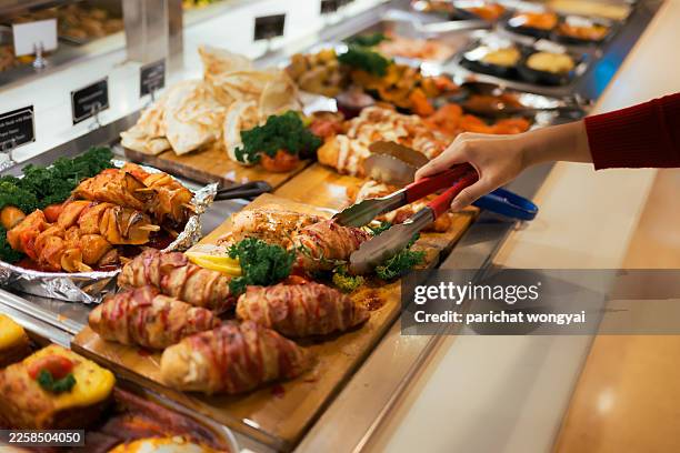 person using tongs to serve from a diverse buffet spread in a catering setting, close-up of hand selecting hot dishes - buffet stockfoto's en -beelden