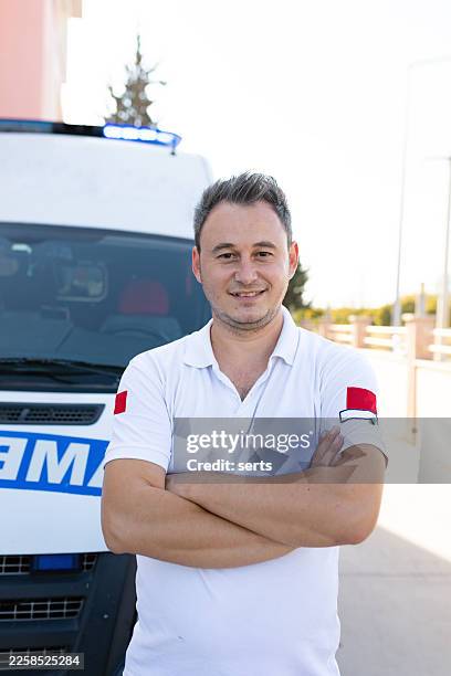 portrait d’un paramédic homme confiant, debout, les bras croisés devant un véhicule ambulancier pendant une mission d’urgence - véhicule de service durgence photos et images de collection
