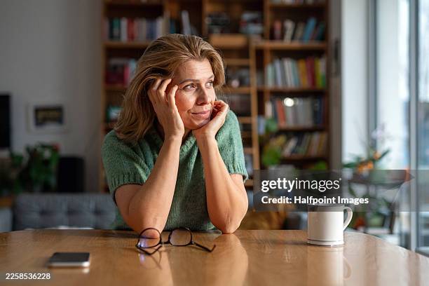 portrait of beautiful mature woman sitting at table. - hand on chin stock pictures, royalty-free photos & images