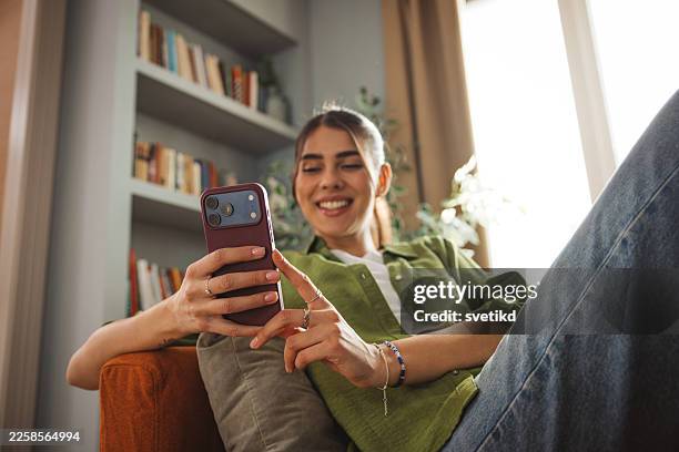 schöne junge frau, die sich zu hause entspannt und ihr smartphone benutzt - in den zwanzigern stock-fotos und bilder