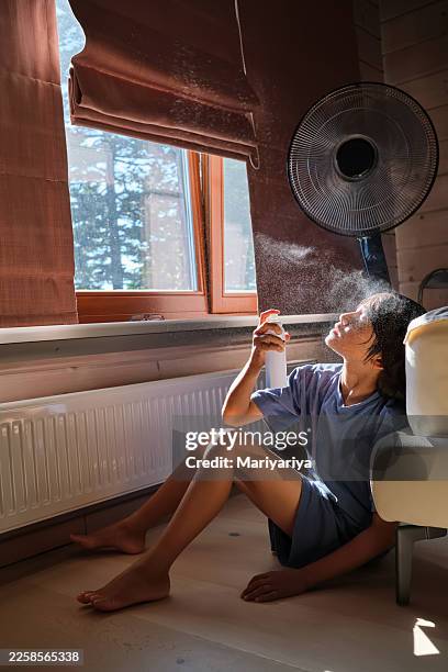 person cooling face with water spray and fan on summer day - hittegolf stockfoto's en -beelden