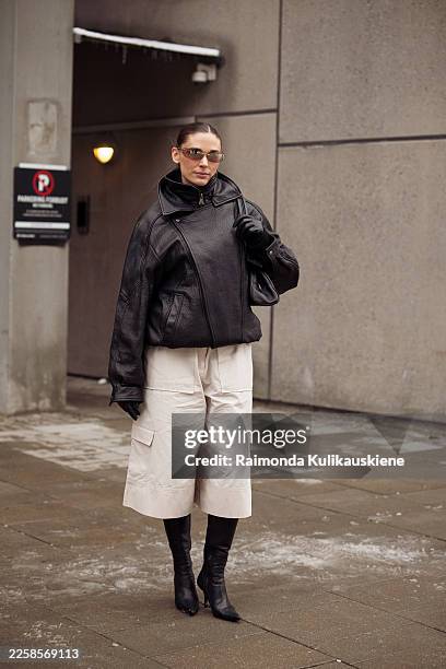 Guest wears black pointy shoes, beige wide shorts, black leather jacket and sunglasses outside the Forza Collective show during Copenhagen Fashion...