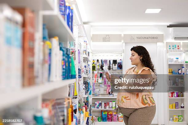 pregnant woman choosing baby products in a pharmacy - woman at pharmacy stock pictures, royalty-free photos & images