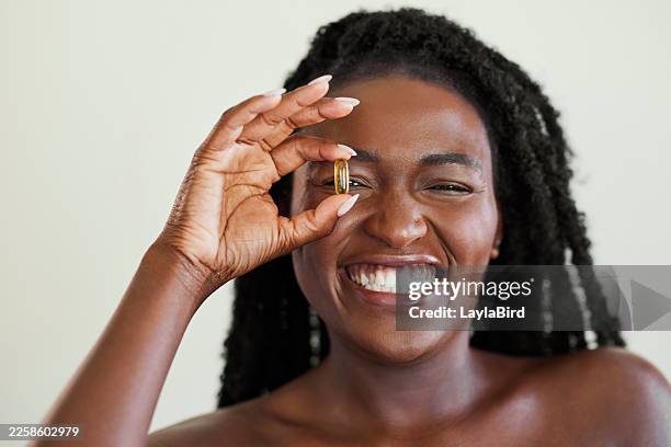 joyful black woman holding vitamin capsule to her eye - omega 3 stock pictures, royalty-free photos & images