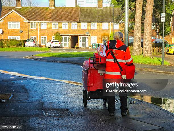female royal mail postal worker pushing mail trolley on residential street - postal worker stock pictures, royalty-free photos & images