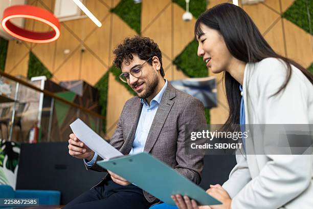 business colleagues review documents in modern office with green wall decor and smiling interaction - pair stock pictures, royalty-free photos & images