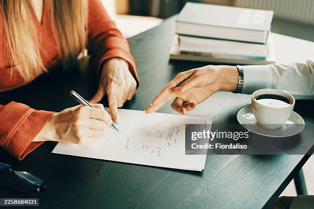 two people collaborate at a table, planning with notes and coffee nearby - erfenis stockfoto's en -beelden
