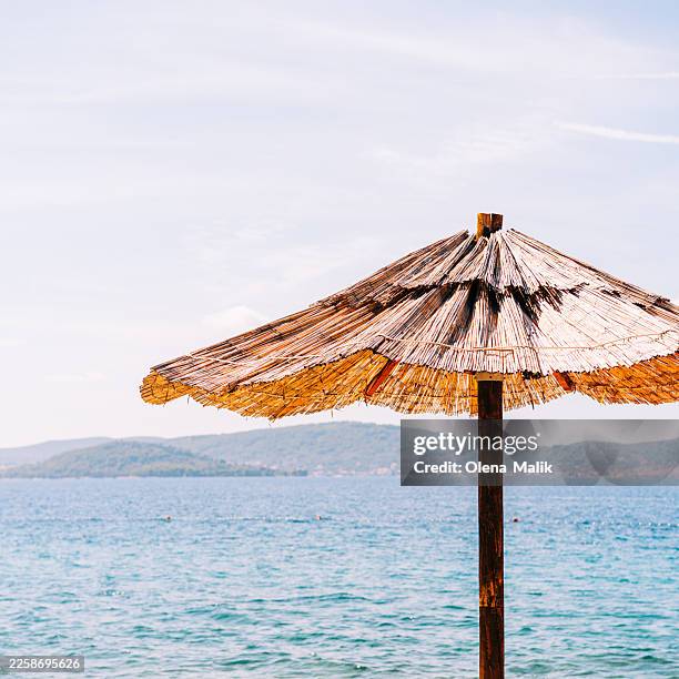 straw beach umbrellas overlooking blue sea on summer day - zadar stock pictures, royalty-free photos & images