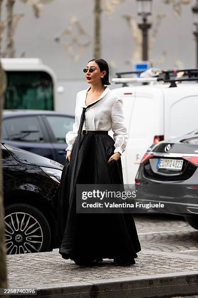 Reem Alswaidi wears black sunglasses, gold earrings, a white shirt and a black maxi long skirt outside Alexis Mabille show during the Haute Couture...
