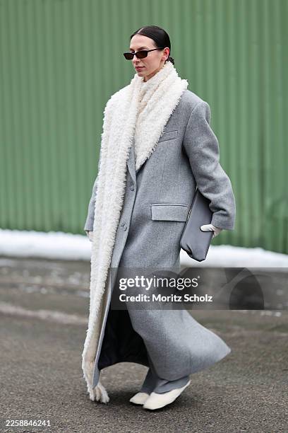 Olga Kurach is seen wearing a long light grey single breasted wool coat „Gigi“ with english spread collar, maxi length welt pockets and a single...