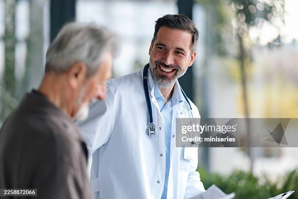 friendly doctor confers with elder patient in clinic corridor, stethoscope around neck during medical checkup - perto imagens e fotografias de stock