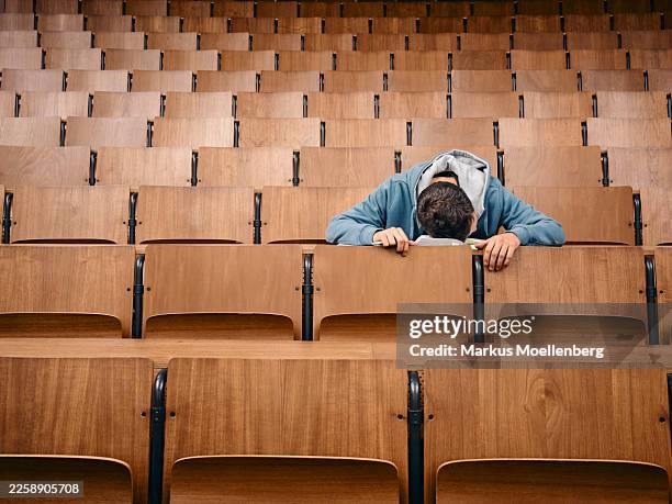 alone student sleeps on desk in empty lecture hall with wooden seats. germany - auditorium stock pictures, royalty-free photos & images