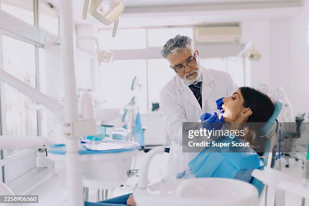 senior male dentist treating female patient in dental clinic - medical procedure stock pictures, royalty-free photos & images