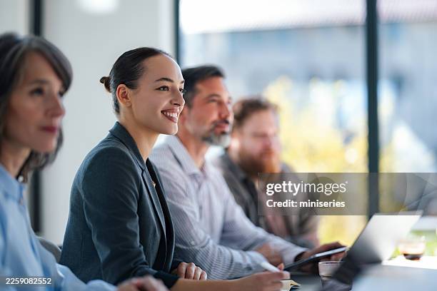 smiling woman leads a professional group in a bright office meeting setting - business talk stock pictures, royalty-free photos & images