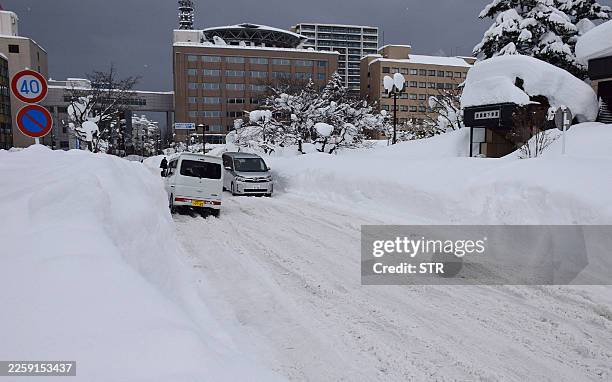 People commute along a snow-covered street in Aomori City on February 3, 2026. Unusually heavy snow in Japan has been blamed for 30 deaths in the...