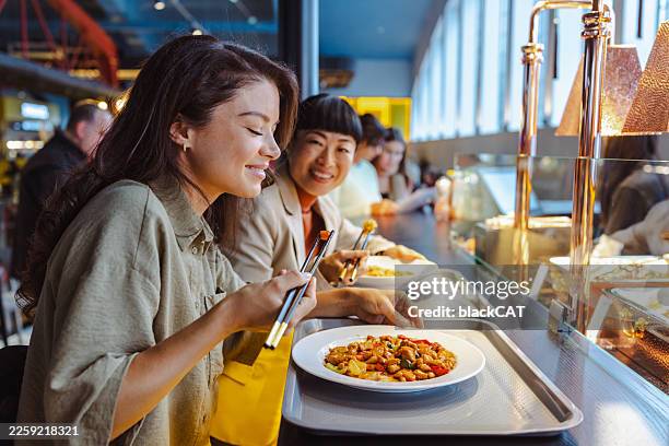diverse female friends enjoy a self-service lunch line, sharing smiles while eating asian dishes - buffet stockfoto's en -beelden