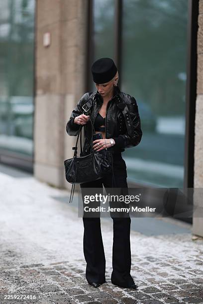 Ava Black seen wearing a black pillbox style hat, cropped black leather jacket by Alexander McQueen, featuring a structured silhouette with bold...