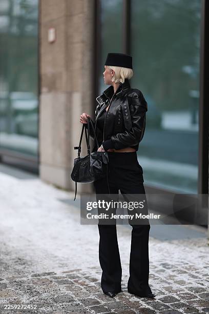 Ava Black seen wearing a black pillbox style hat, cropped black leather jacket by Alexander McQueen, featuring a structured silhouette with bold...