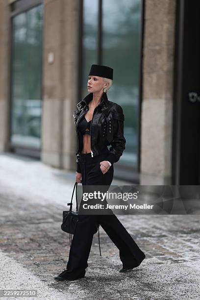 Ava Black seen wearing a black pillbox style hat, cropped black leather jacket by Alexander McQueen, featuring a structured silhouette with bold...
