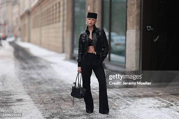 Ava Black seen wearing a black pillbox style hat, cropped black leather jacket by Alexander McQueen, featuring a structured silhouette with bold...