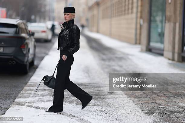 Ava Black seen wearing a black pillbox style hat, cropped black leather jacket by Alexander McQueen, featuring a structured silhouette with bold...