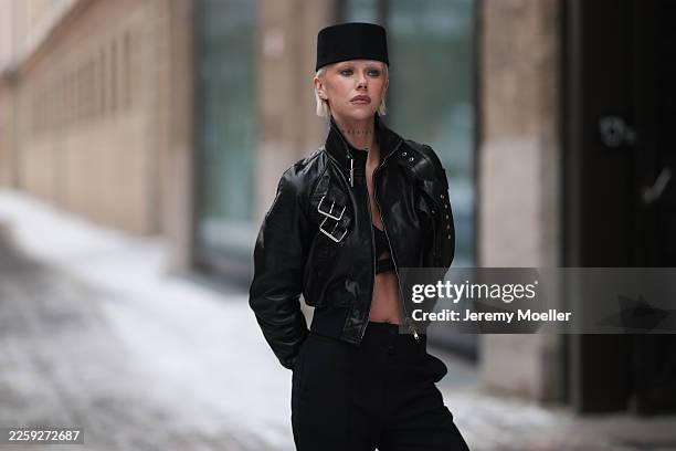 Ava Black seen wearing a black pillbox style hat, a cropped black leather jacket by Alexander McQueen, featuring a structured silhouette with bold...