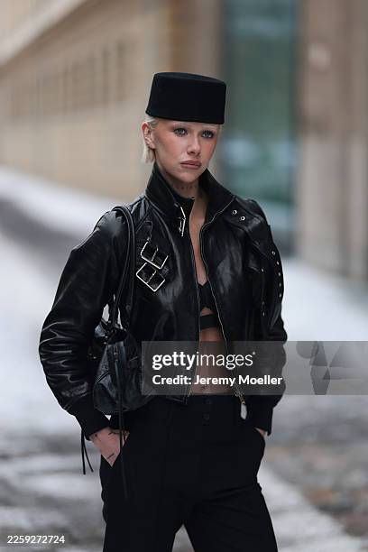Ava Black seen wearing a black pillbox style hat, a cropped black leather jacket by Alexander McQueen, featuring a structured silhouette with bold...