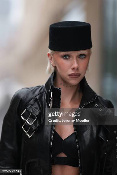 Ava Black seen wearing a black pillbox style hat, a cropped black leather jacket by Alexander McQueen, featuring a structured silhouette with bold...