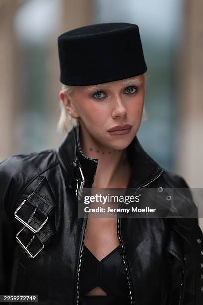 Ava Black seen wearing a black pillbox style hat, a cropped black leather jacket by Alexander McQueen, featuring a structured silhouette with bold...
