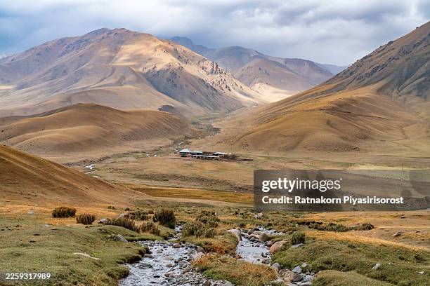 ground-level view of a small mountain settlement and winding stream in a high-altitude valley of rural kyrgyzstan during morning. - foothills stock pictures, royalty-free photos & images