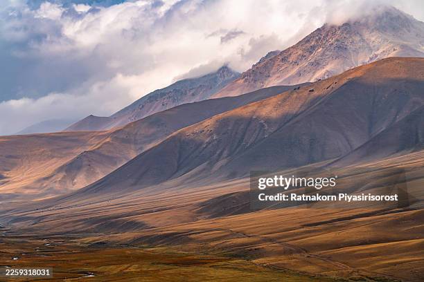 ground-level view of a small mountain settlement and winding stream in a high-altitude valley of rural kyrgyzstan during morning. - foothills stock pictures, royalty-free photos & images
