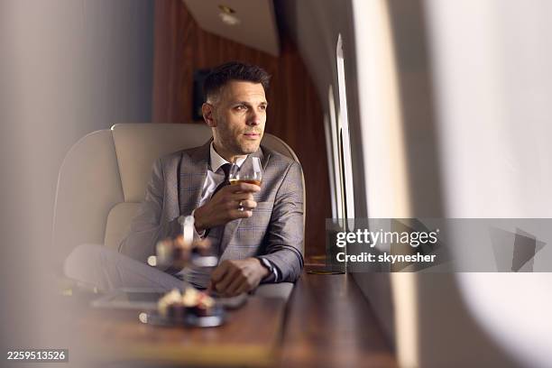 thoughtful businessman drinking whiskey during flight in corporate jet. - billionaire stock pictures, royalty-free photos & images