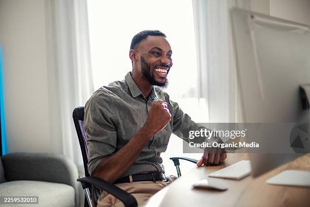 african man celebrating success working on computer at home - good news stock pictures, royalty-free photos & images
