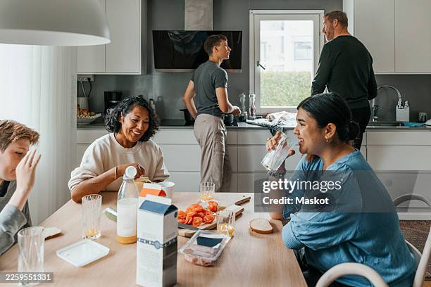 smiling young woman drinking milk while sitting with family for breakfast at home - milk carton stock pictures, royalty-free photos & images