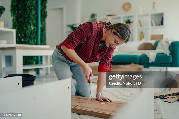 jeune femme assemblant des meubles en format plat à la maison, construisant de nouvelles étagères, créant de nouveaux espaces de vie - tournevis photos et images de collection