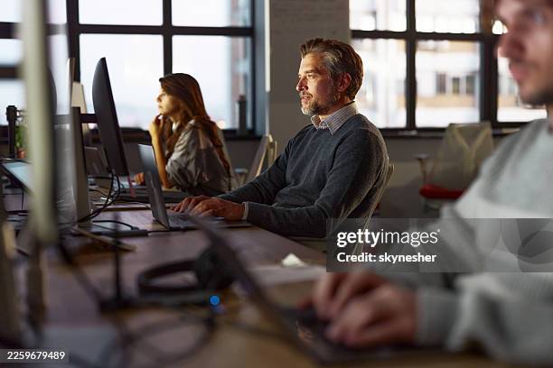 male programmer using laptop while working on pc in the office. - programmer working stock pictures, royalty-free photos & images