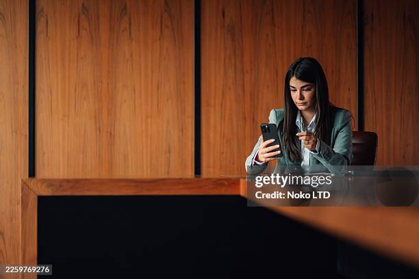 professional businesswoman sitting at office desk, checking messages on smartphone, connecting with colleagues and clients - electric skateboard stock pictures, royalty-free photos & images