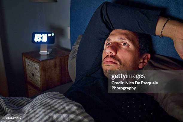 man awake in bed staring into space during sleepless night - digital clock face stock pictures, royalty-free photos & images